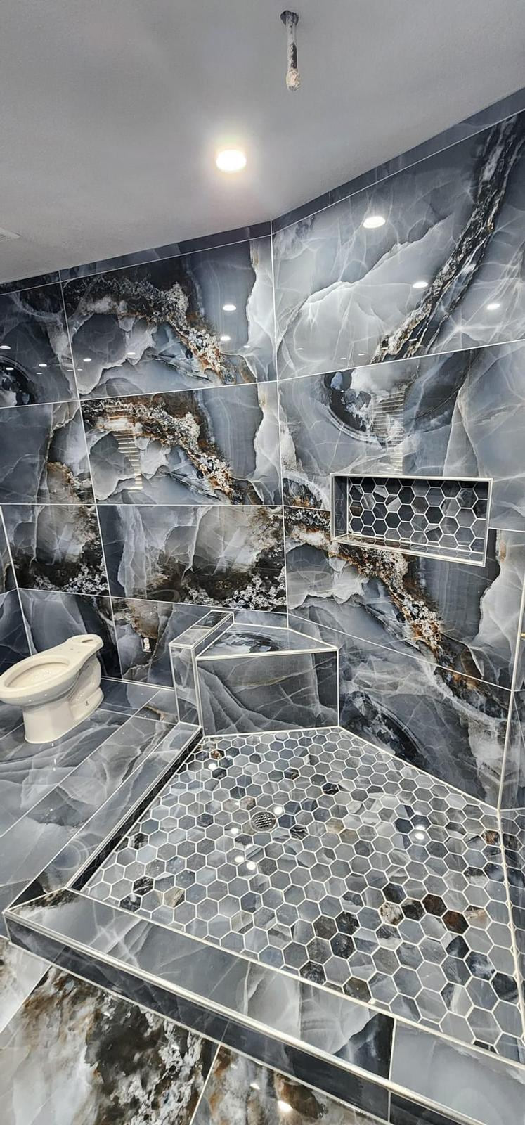 Gray veined shower under construction with a hex mosaic floor, built-in bench and recessed niche